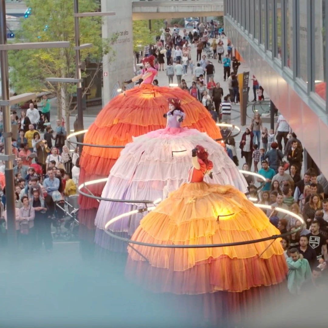 Artistas sobre zancos con vestidos gigantes de tul naranja y rosa, actuando ante una multitud, en Portugal