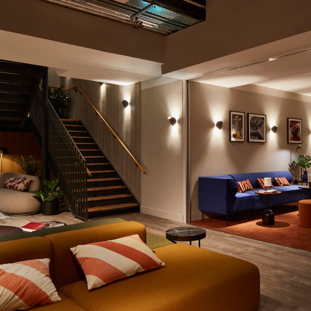 Zona de estar de hotel por la noche, con sofá azul, sofá mostaza y escalera