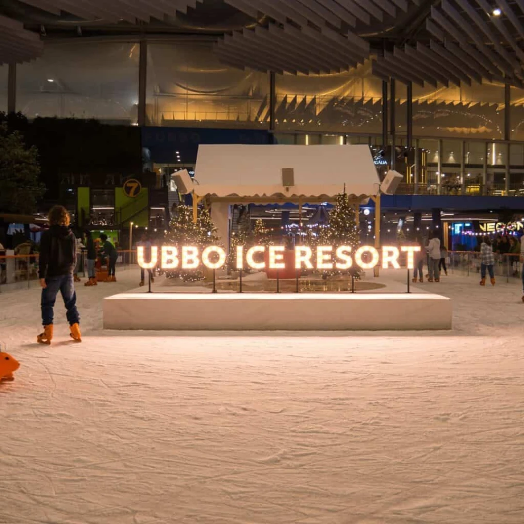 Pista de hielo nocturna con el rótulo iluminado "Ubbo Ice Resort" y un patinador
