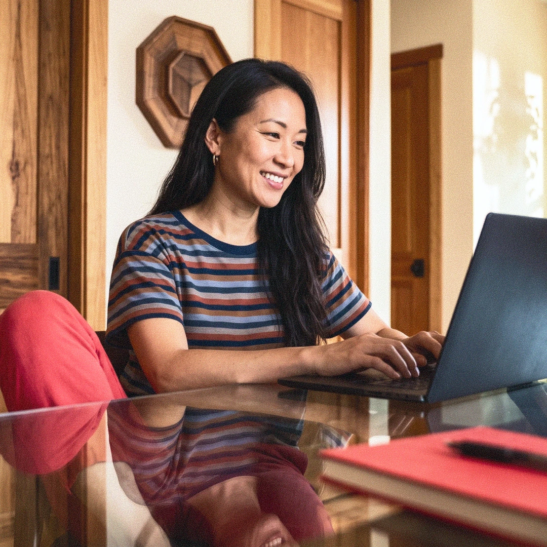 mujer asiática sonriente sentada de forma informal y trabajando delante del ordeandor