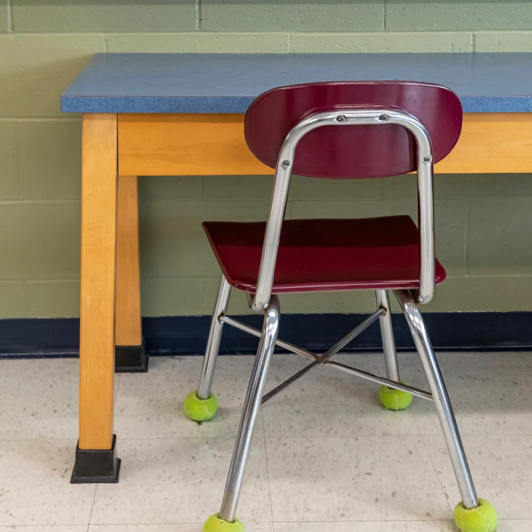 Silla de aula con pelotas de tenis en las patas, frente a una pizarra
