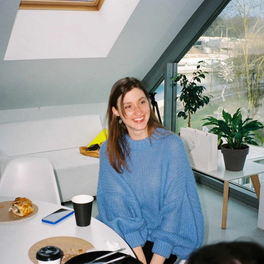 Imagen de una chica vestida con un jersey de color azul, sentada en una mesa dentro de una habitación de color blanco.