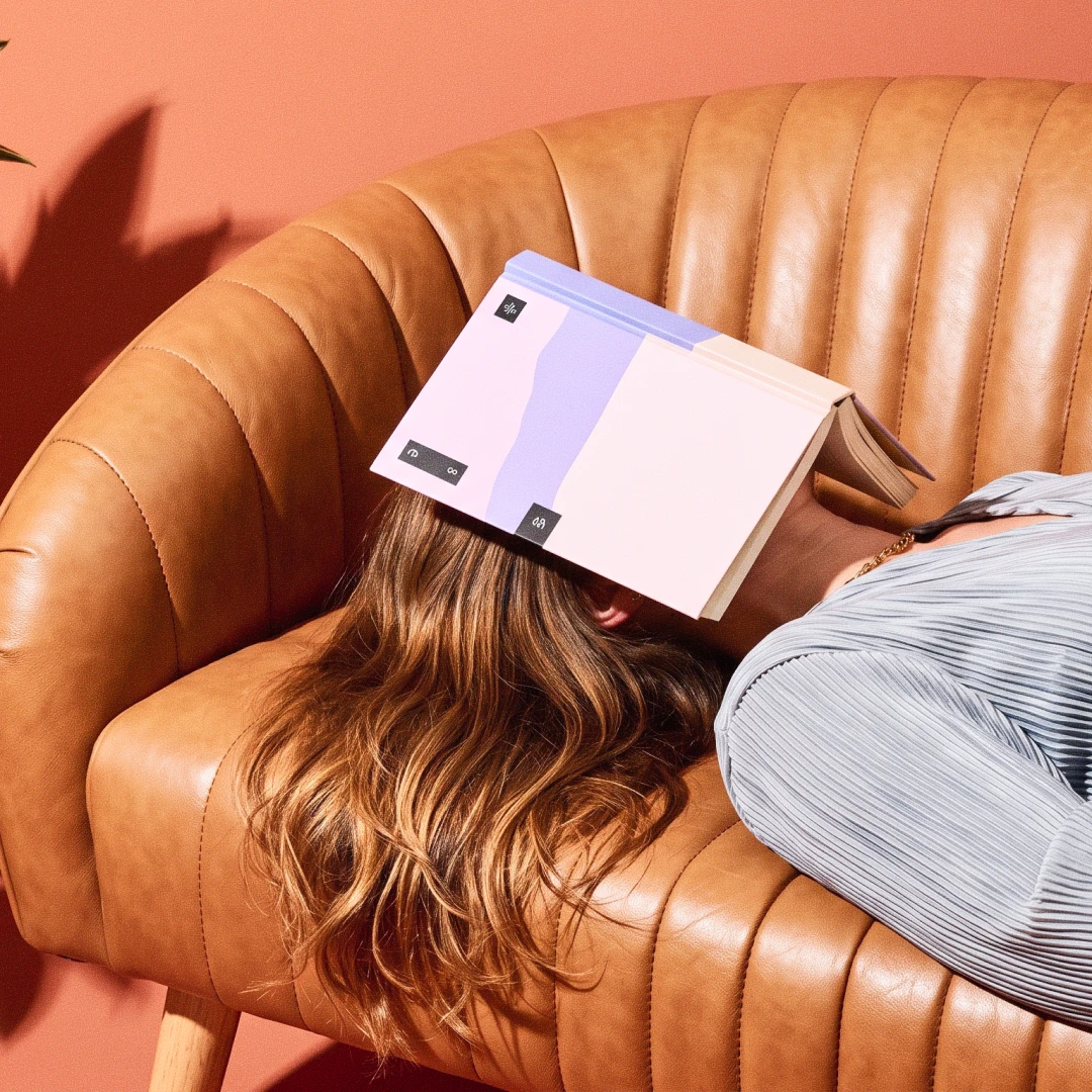Mujer tumbada en un sofá con un libro abierto cubriéndole la cara, en una pausa de lectura